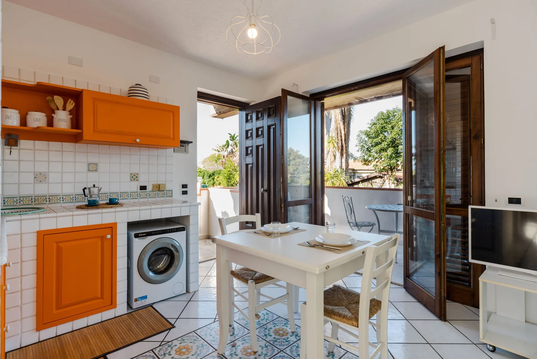Comedor con una mesa blanca junto a una cocina abierta y puertas al balcón.