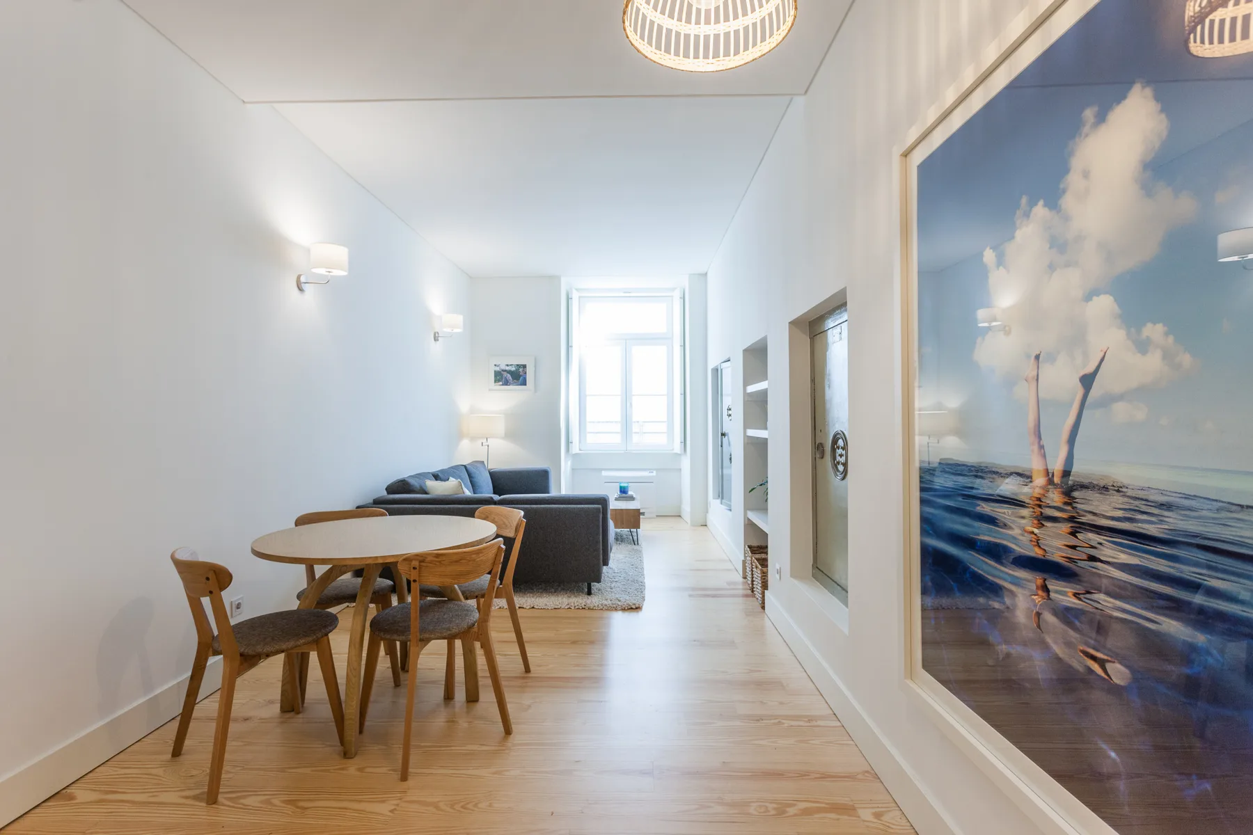 A bright living and dining area features a round table and large ocean-themed artwork.