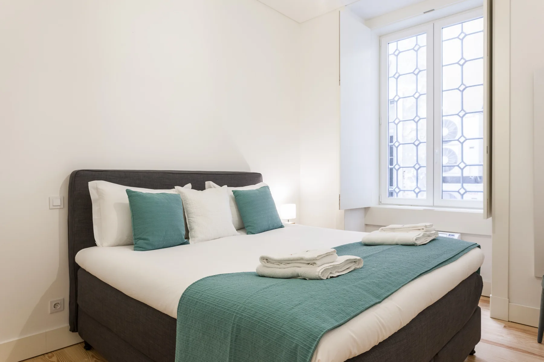 A bright bedroom with a bed dressed in white linens and teal accents.