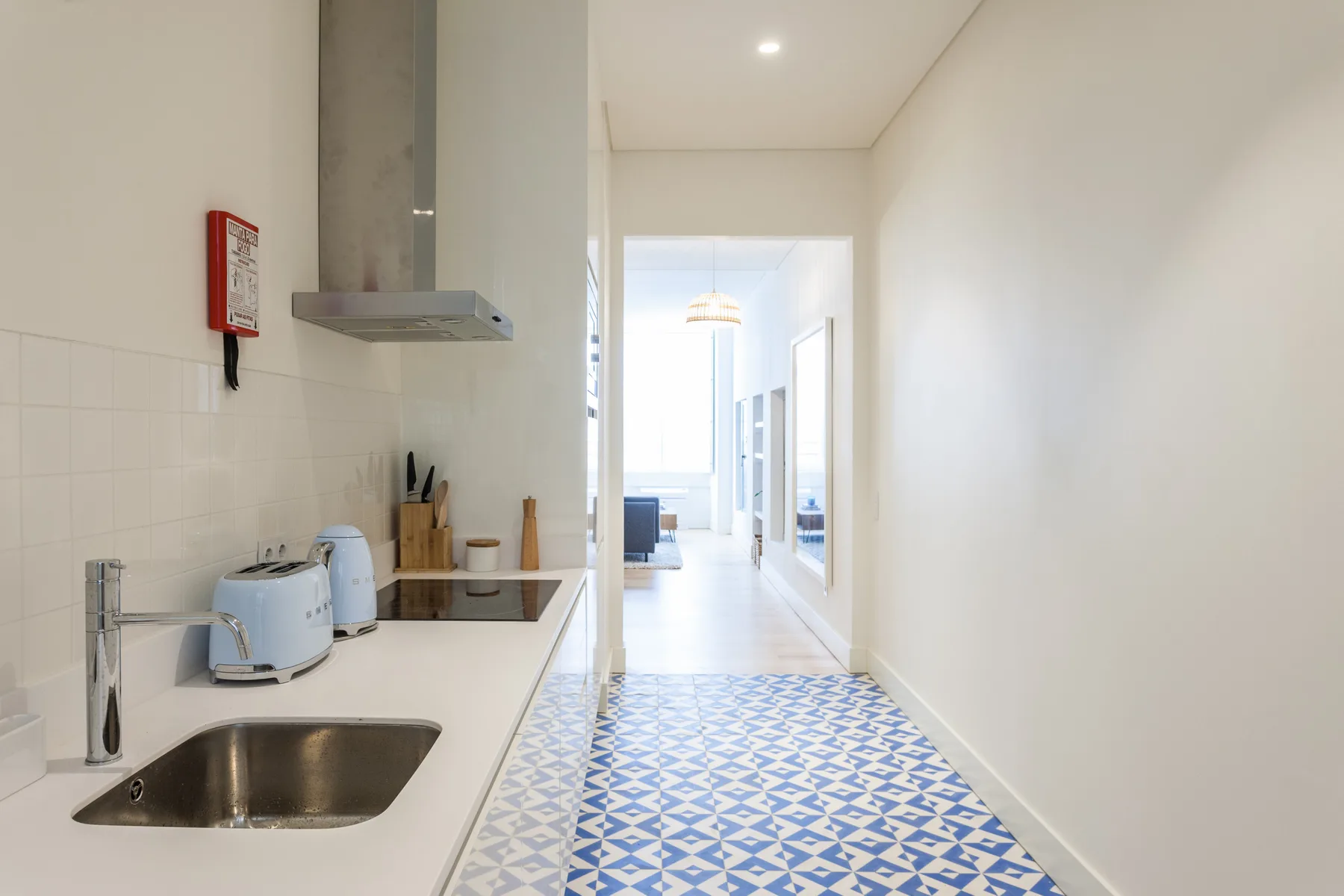 A bright kitchen opens onto a long hallway with patterned floor tiles.