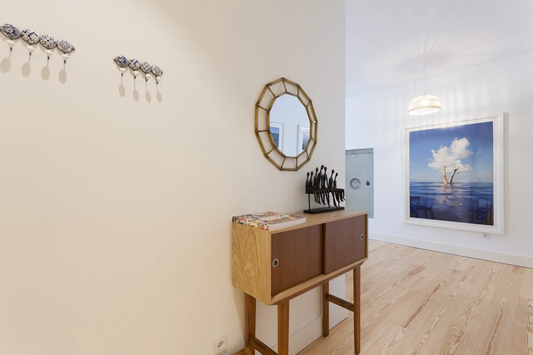 A bright interior with a wooden console, wall mirror, and framed ocean artwork.