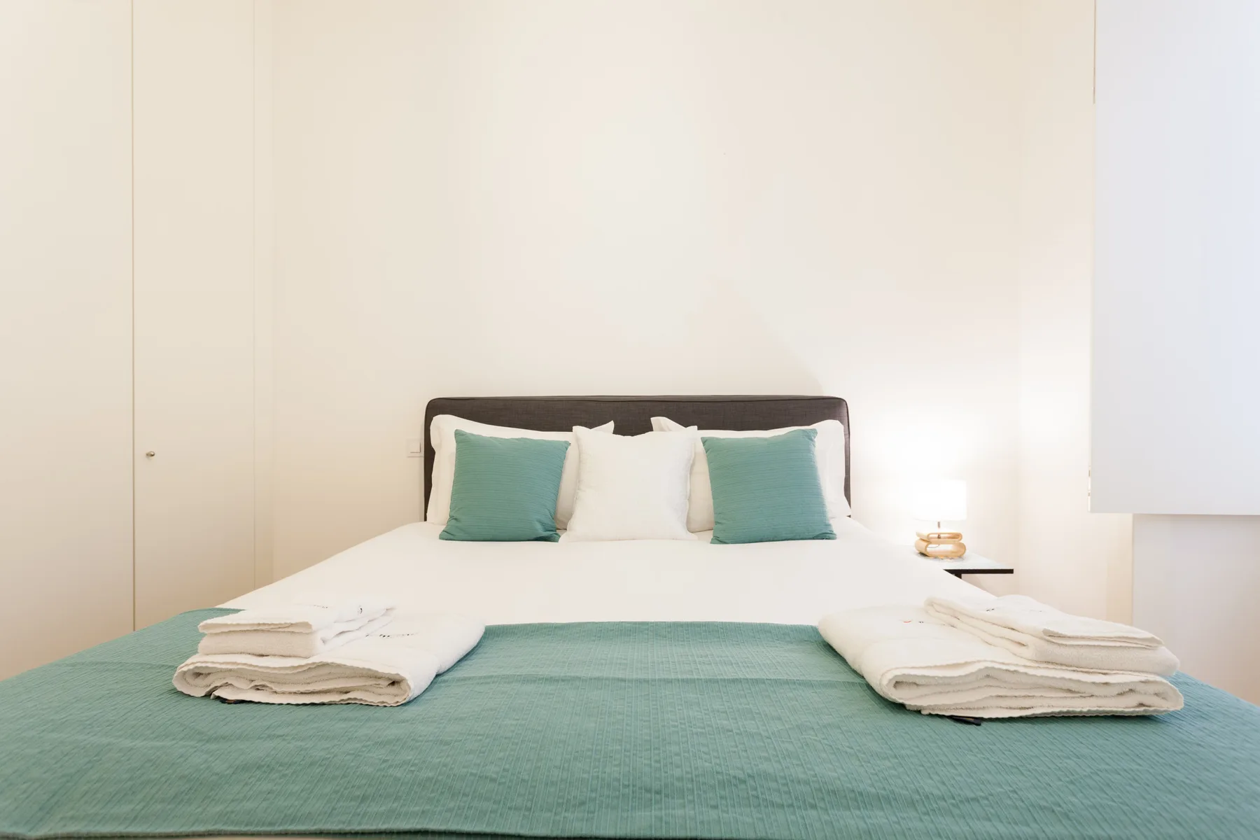 A neatly made bed with turquoise bedding and folded towels in a bedroom.