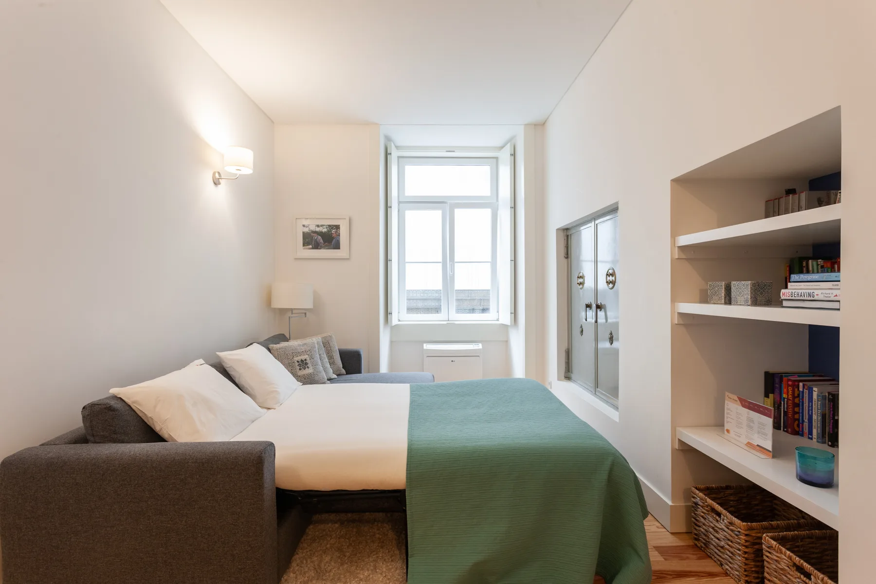 A bright bedroom with a bed, green coverlet, and built-in shelves.