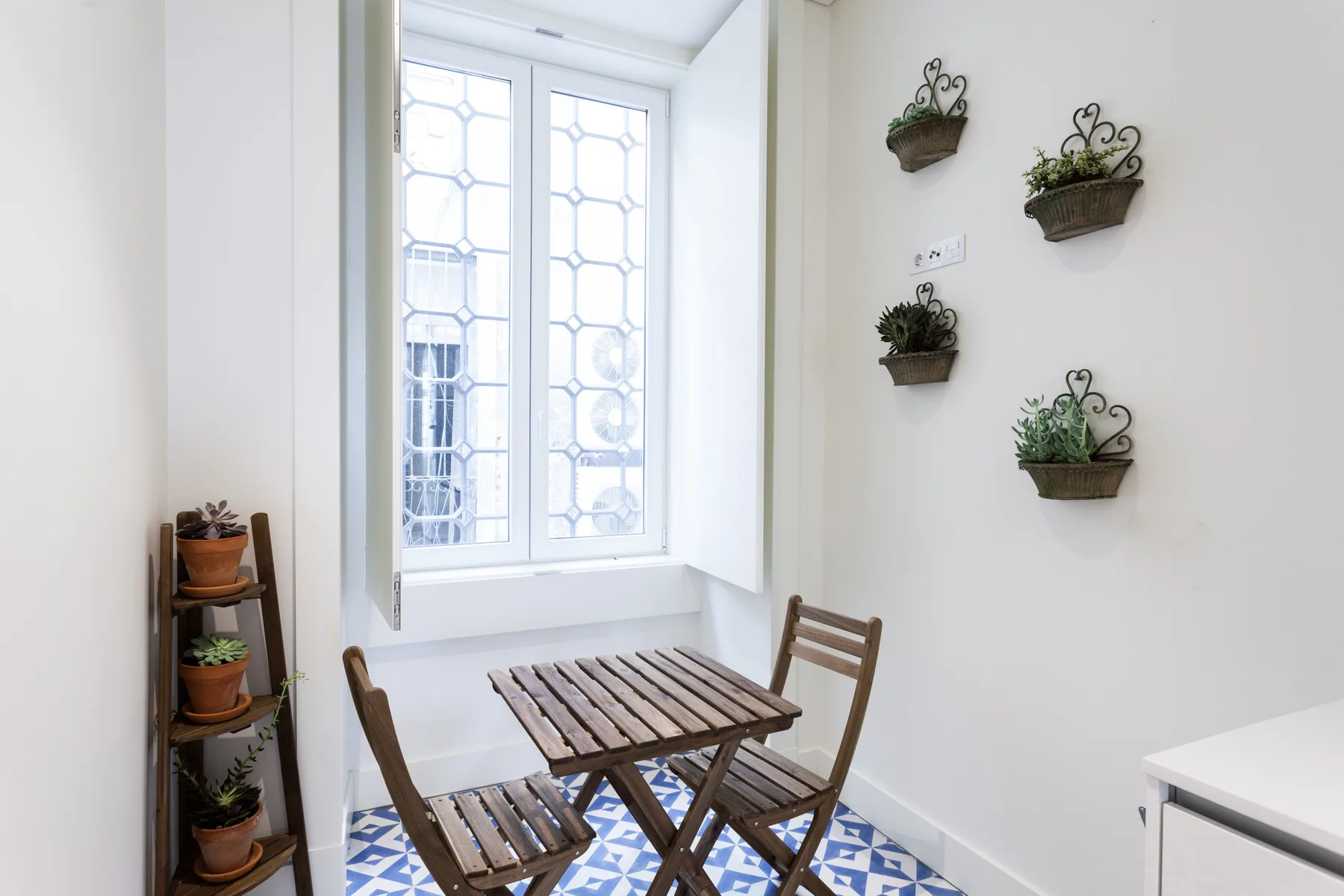 Un pequeño comedor con asientos de madera, una mesa y plantas en macetas.
