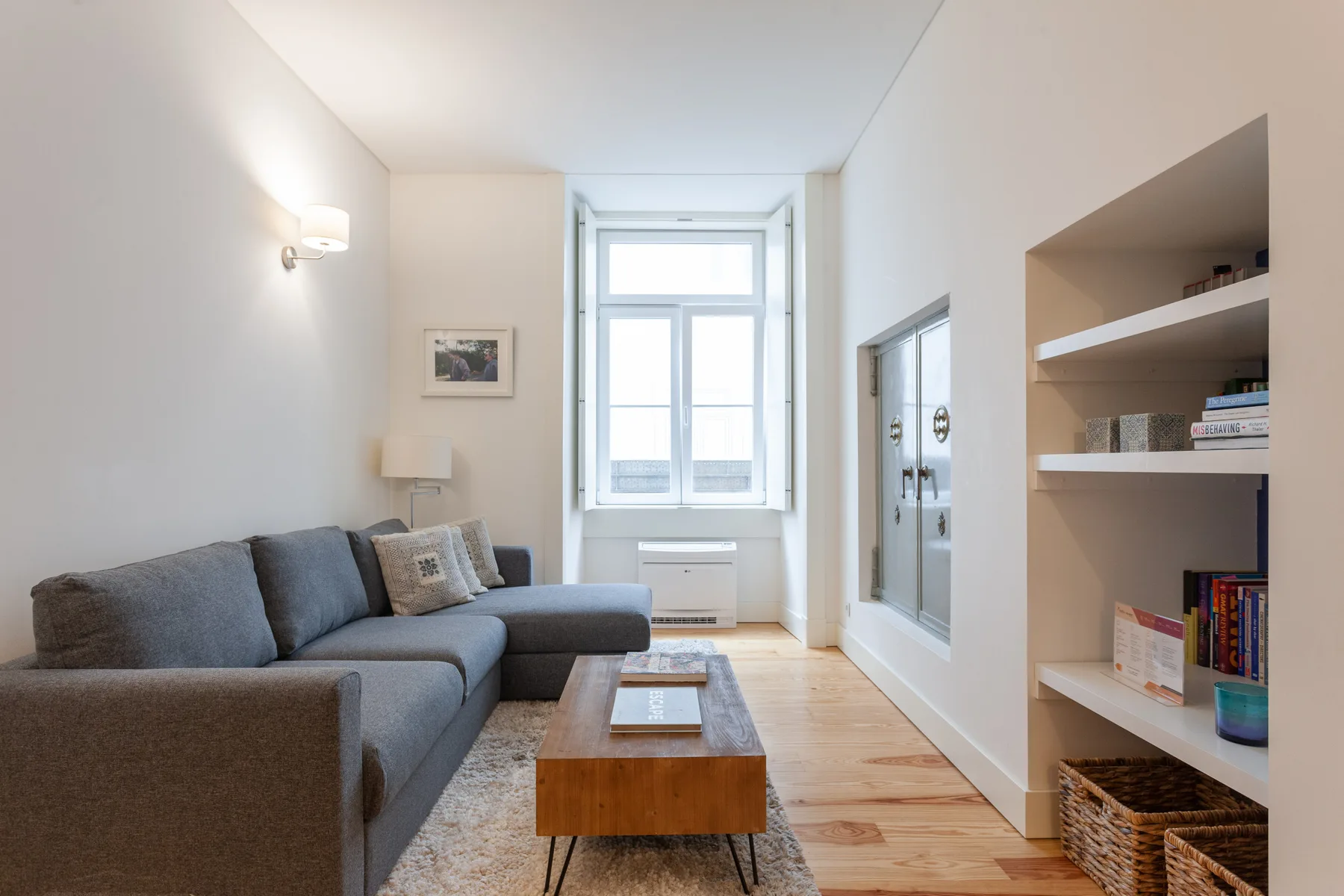 Una sala de estar luminosa con un sofá seccional gris y estanterías empotradas.