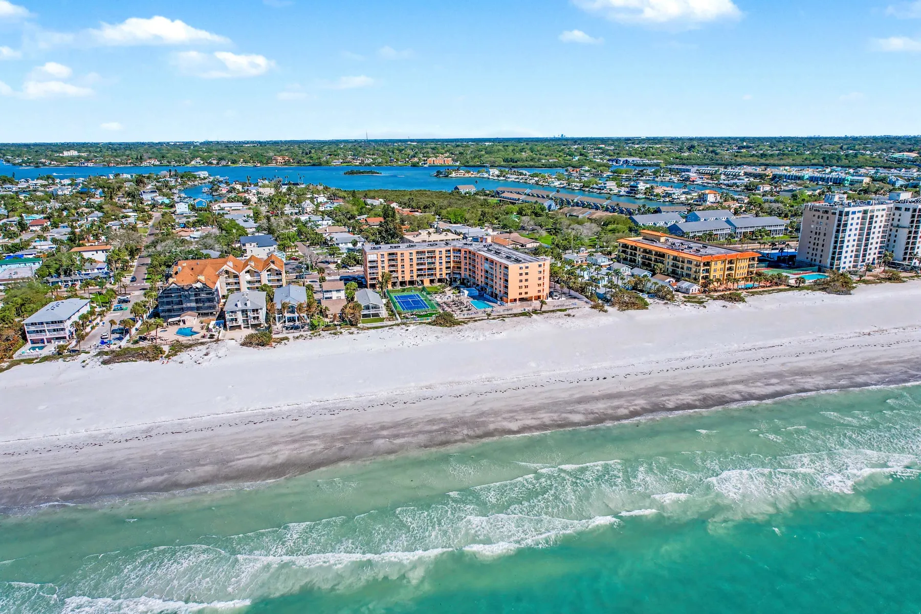 Aerial view of a coastal neighborhood beside a sandy beach and turquoise water.