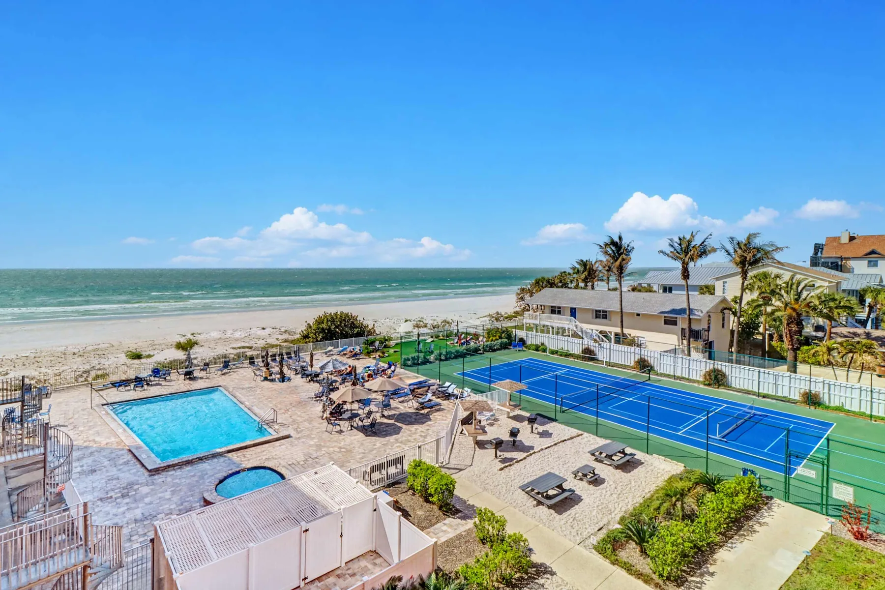 Aerial view of a beachfront pool and tennis courts beside the ocean.