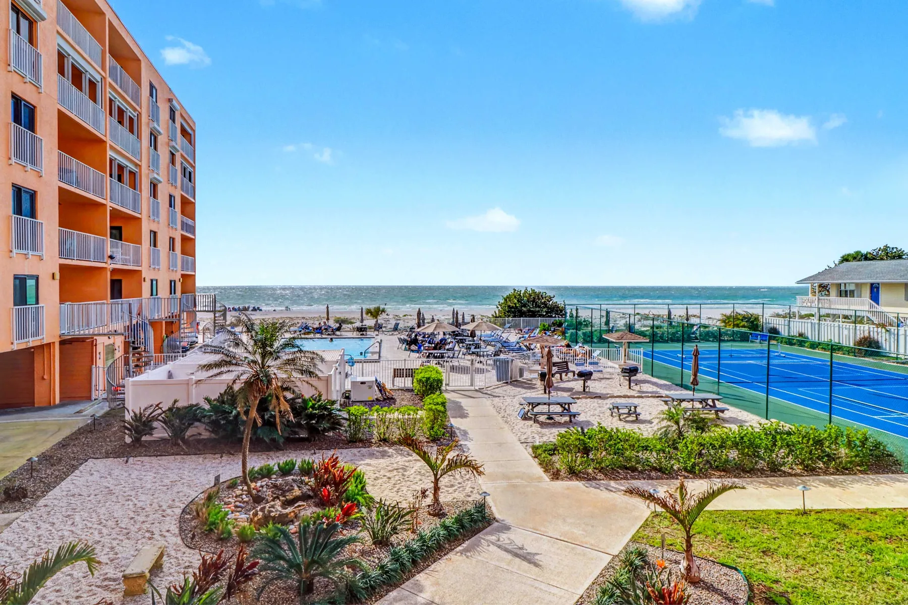 A seaside resort courtyard has landscaped paths, a pool, and tennis courts.