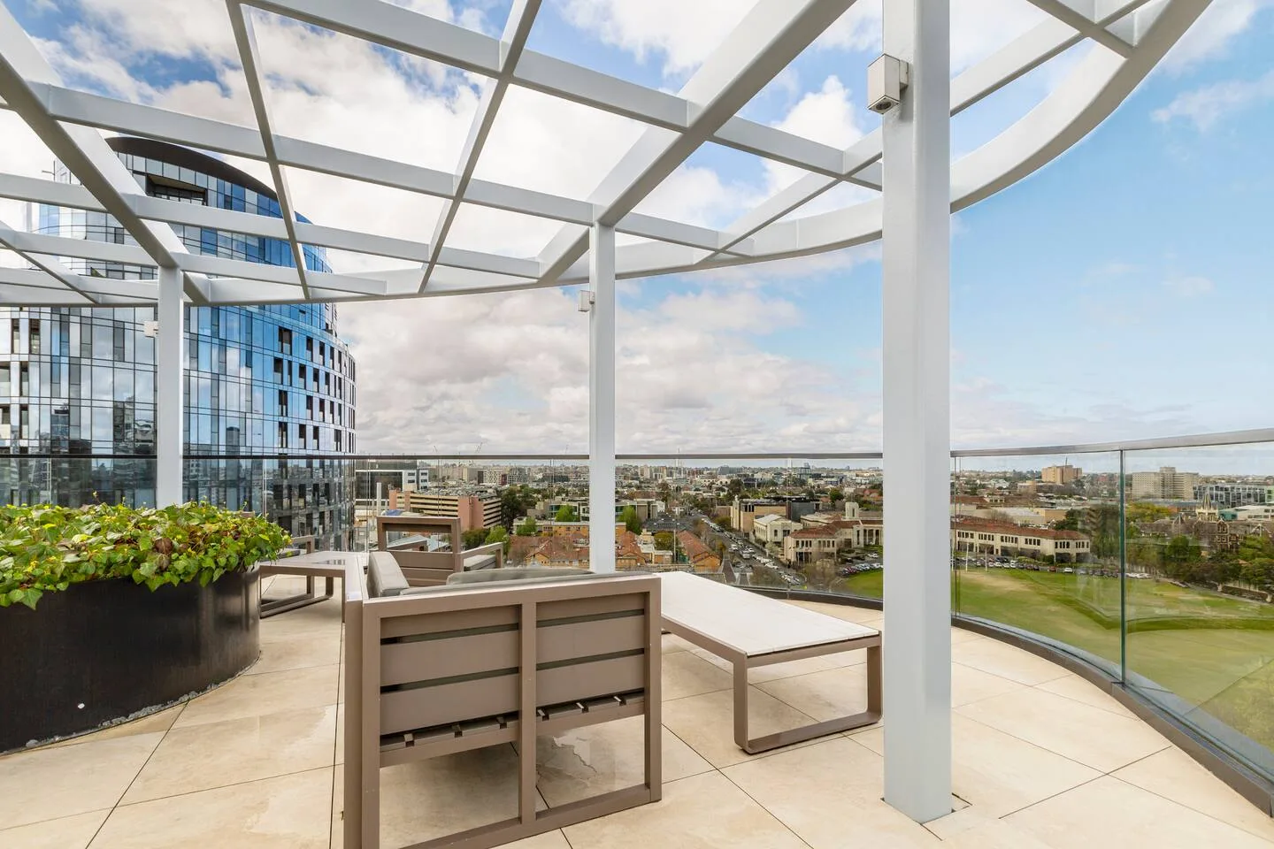 A rooftop terrace has outdoor seating beneath an open white canopy, overlooking the city.
