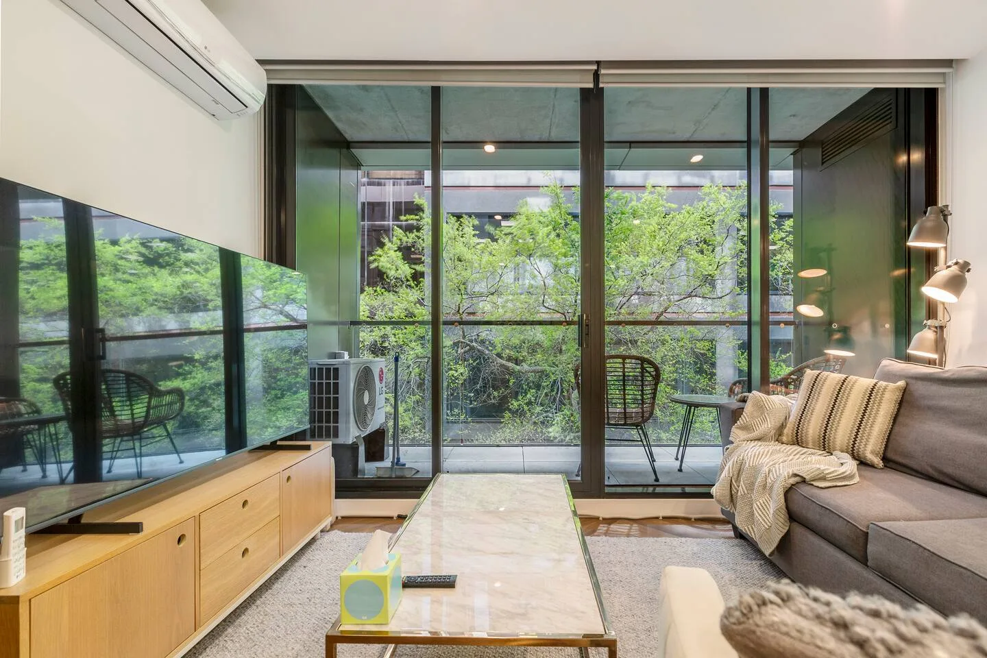 A living room with seating beside floor-to-ceiling windows overlooking greenery.