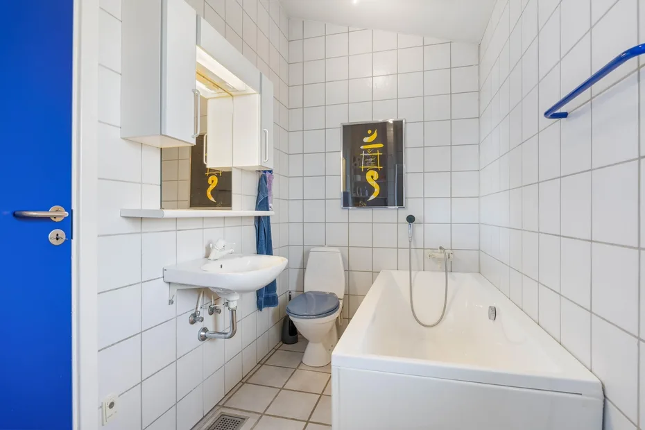 Un baño alicatado con bañera, inodoro y lavabo suspendido.