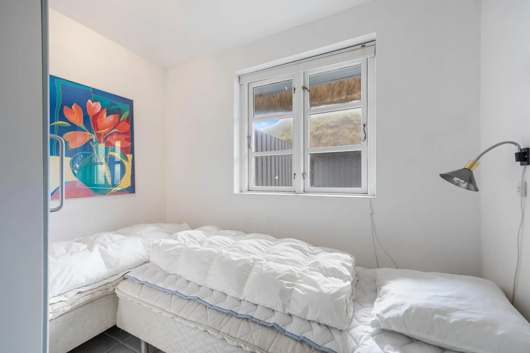 Dormitorio con una cama bajo una ventana y arte colorido en la pared.