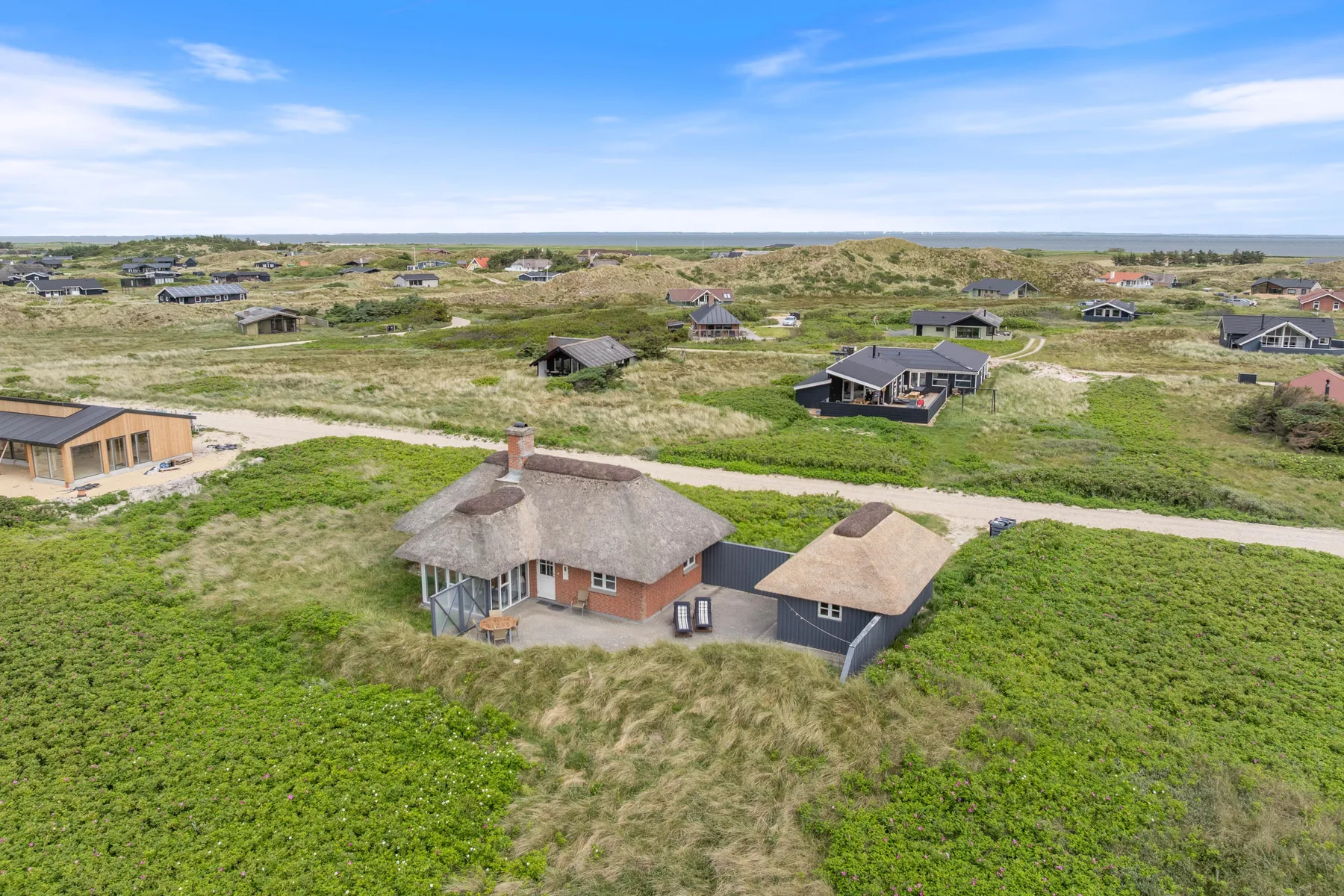 Vista aérea de una casa con techo de paja entre vegetación baja y casas vecinas.