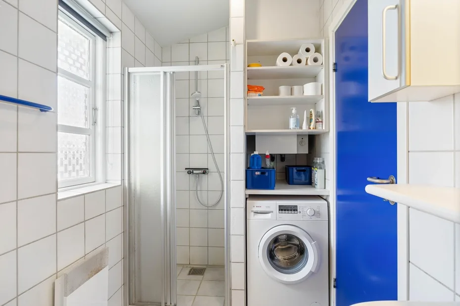 Un baño alicatado con ducha, lavadora y estantes abiertos.