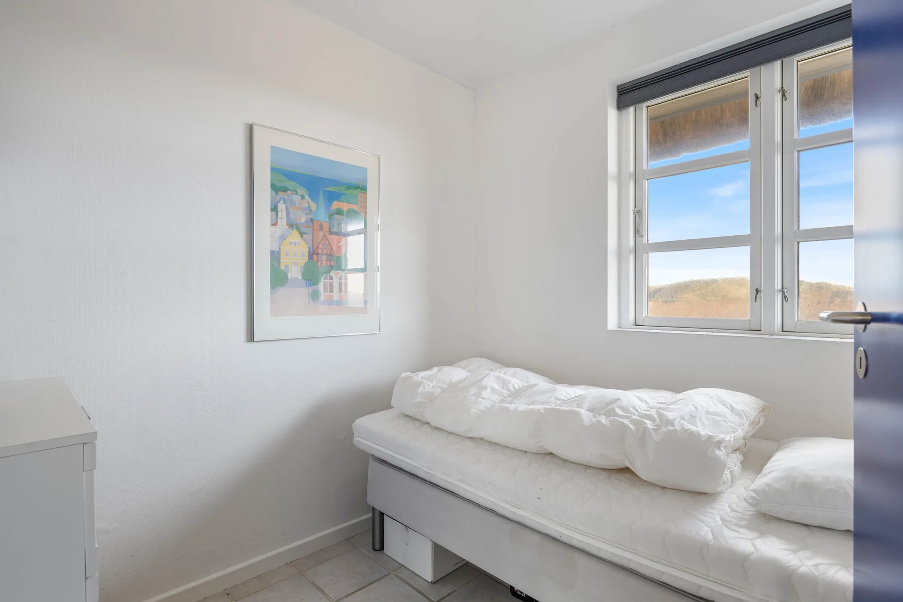 Un dormitorio luminoso con una cama blanca junto a una ventana.