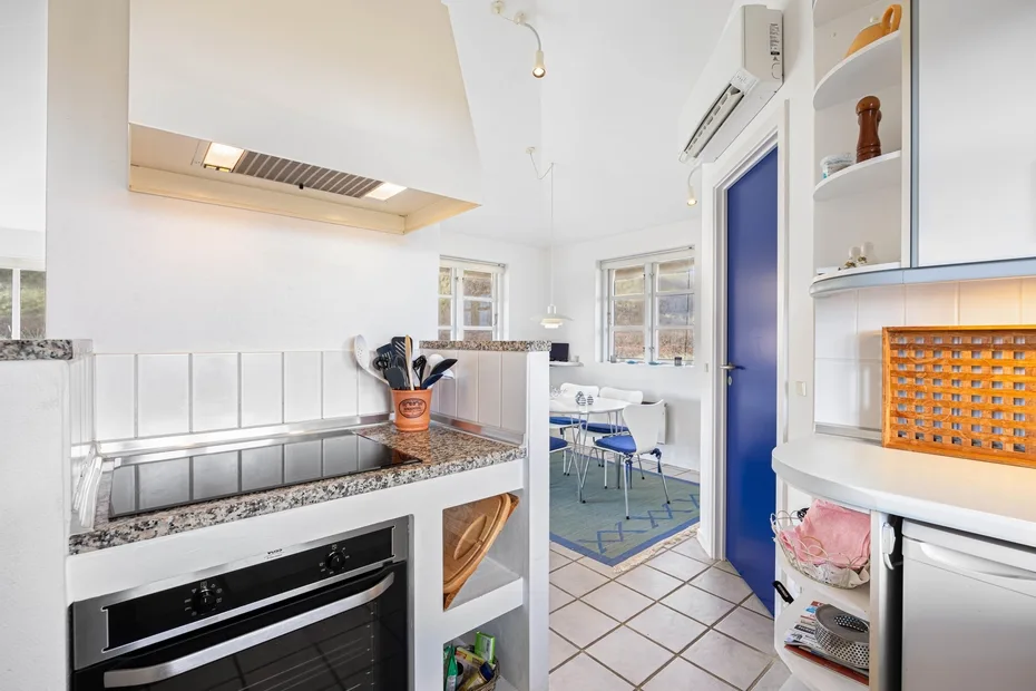 Una cocina luminosa con encimera, horno empotrado y una mesa de comedor al fondo.