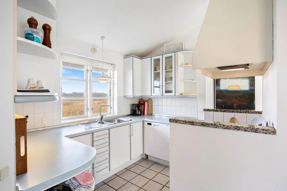 Una cocina luminosa con gabinetes blancos, piso de baldosas y una ventana grande.