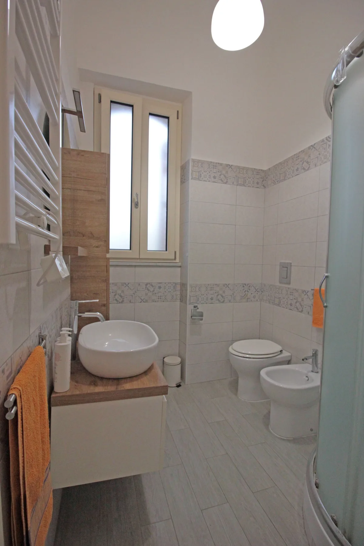 A tiled bathroom with a sink, toilet, bidet, and window.