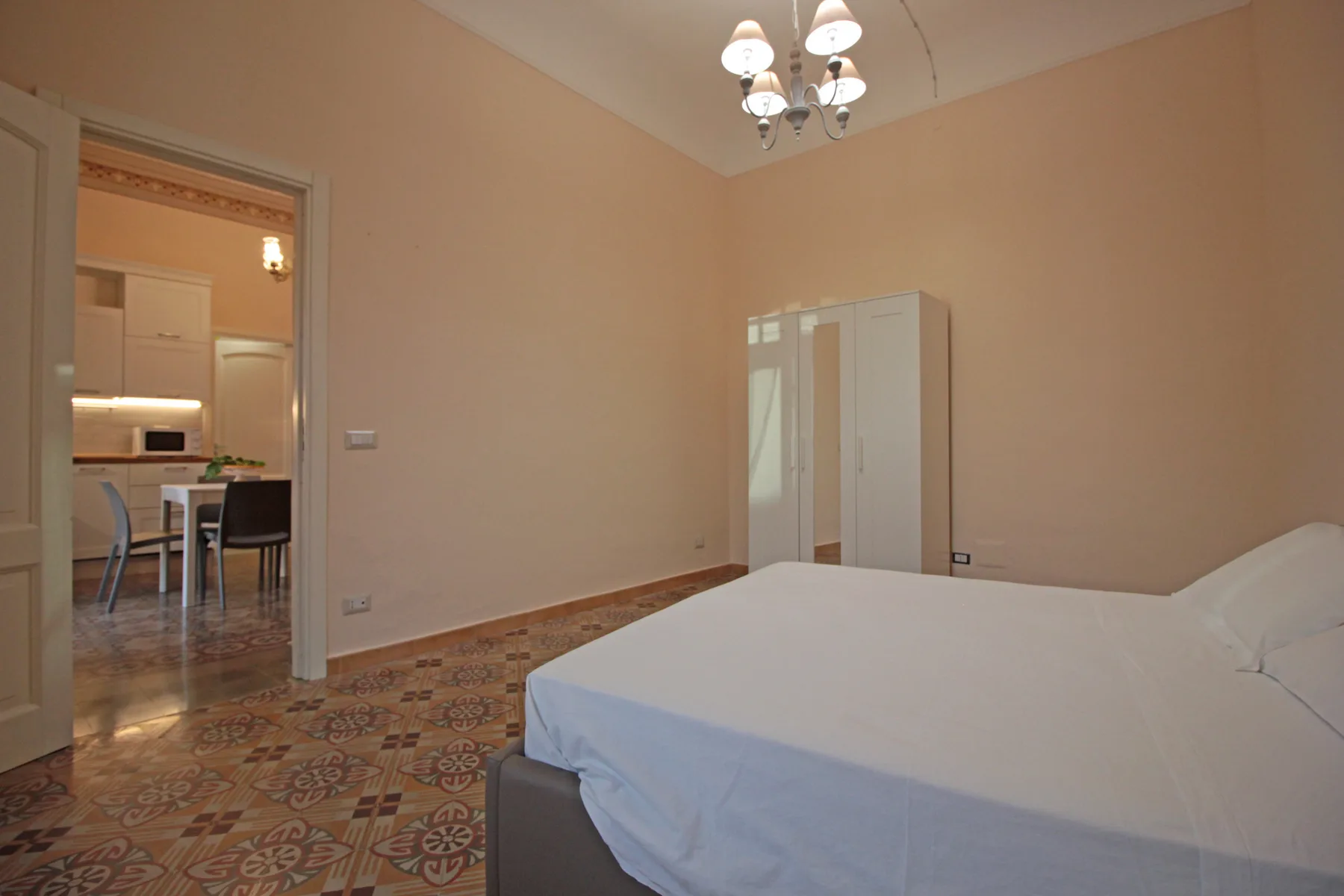 A bedroom with a bed, wardrobe, and an adjoining kitchen visible through the doorway.