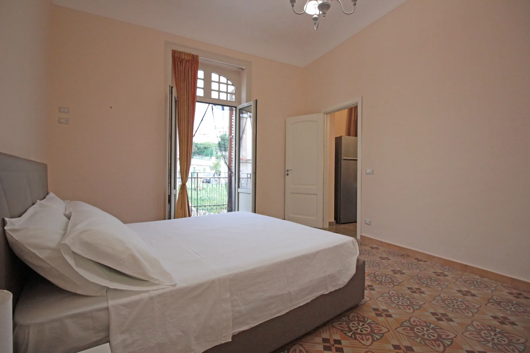 A bedroom with a neatly made bed beside a tall window.