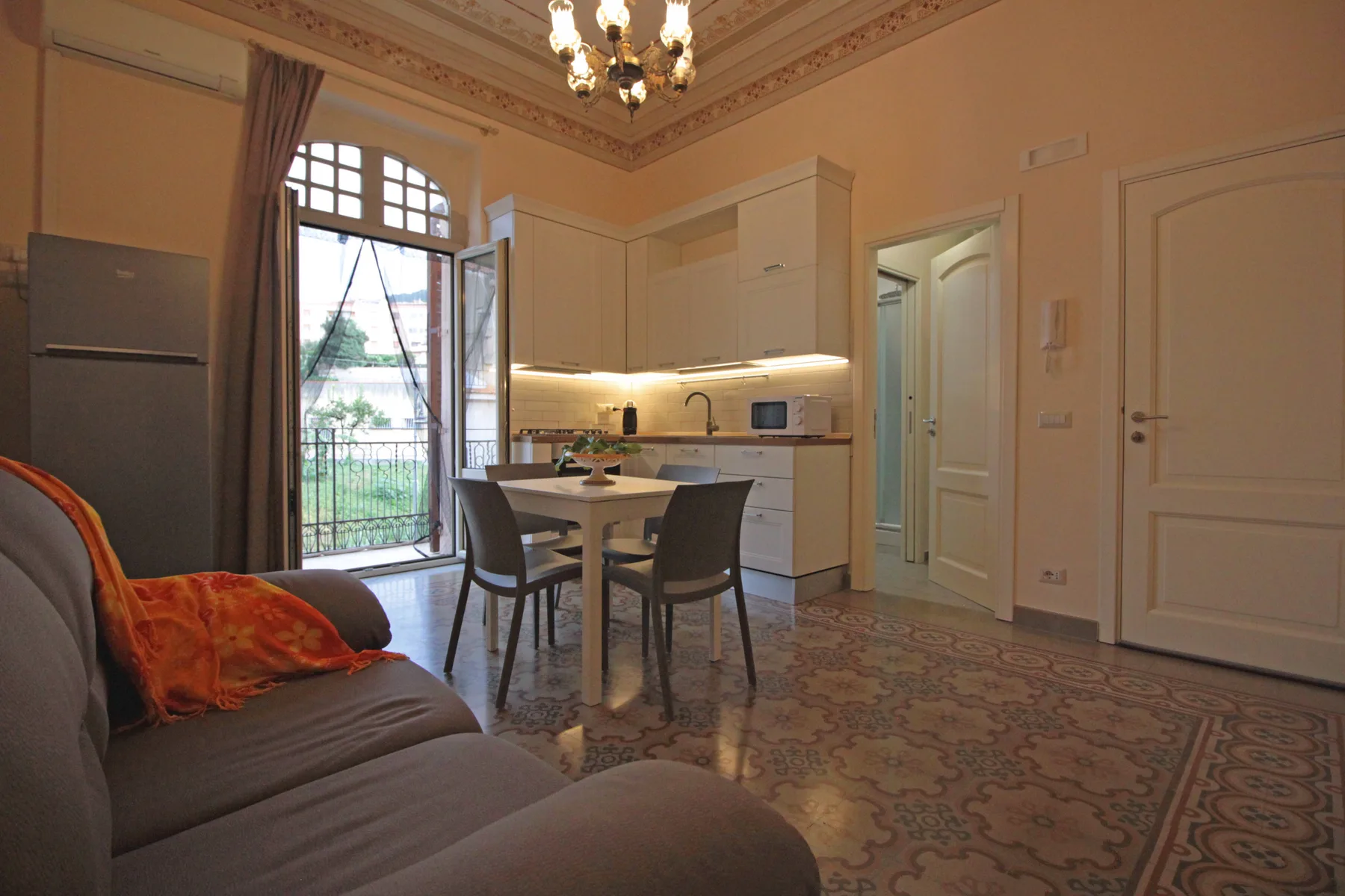 A living and dining area with a compact kitchen and tall windows.