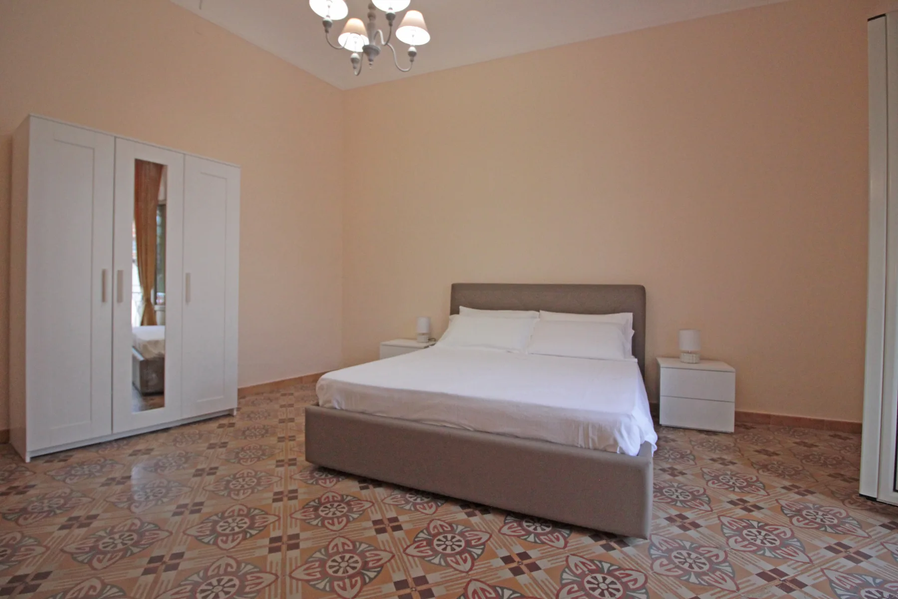 A bedroom with a bed, wardrobe, and patterned tile floor.