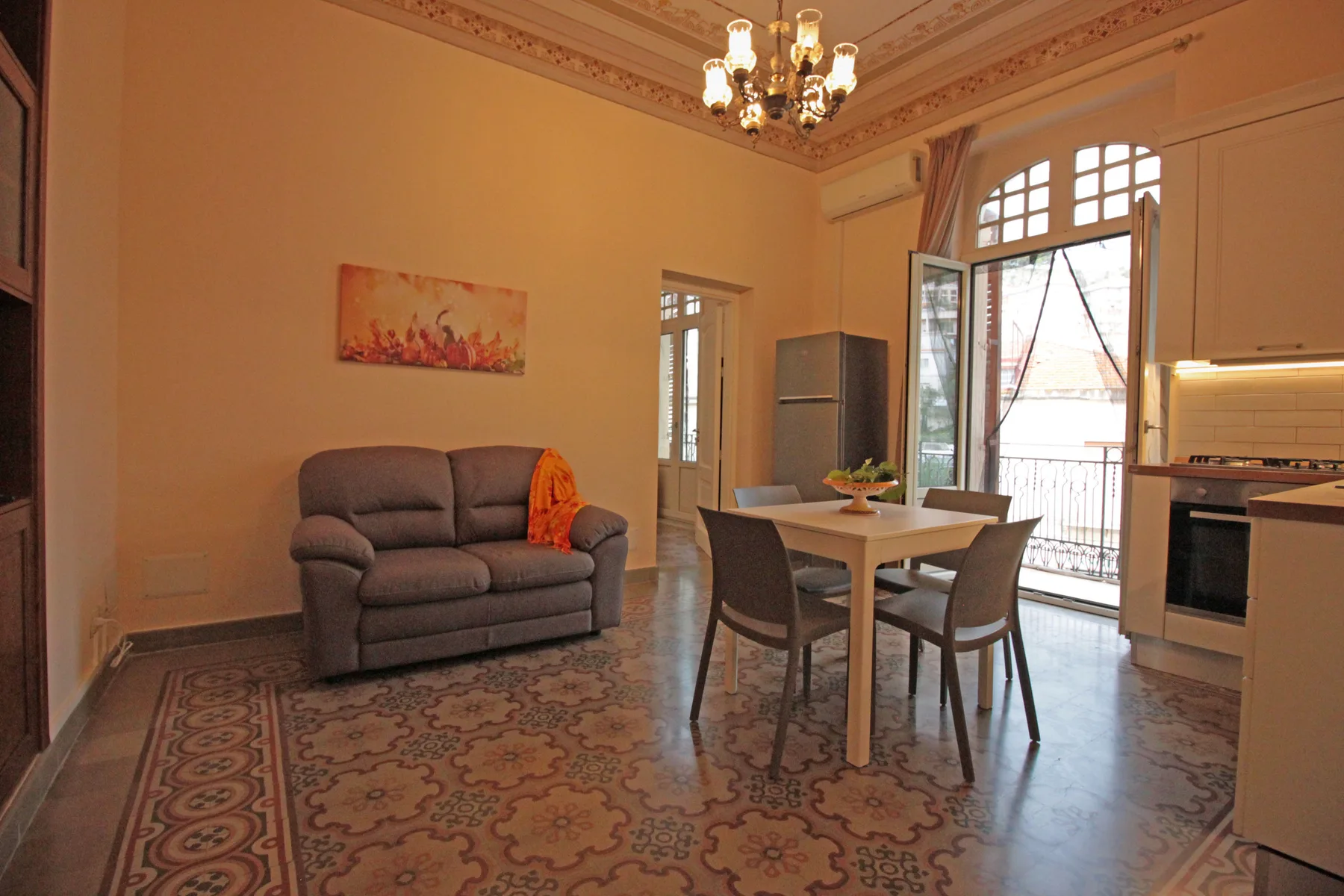 A dining area with a table and chairs sits beside an open kitchen and tall windows.