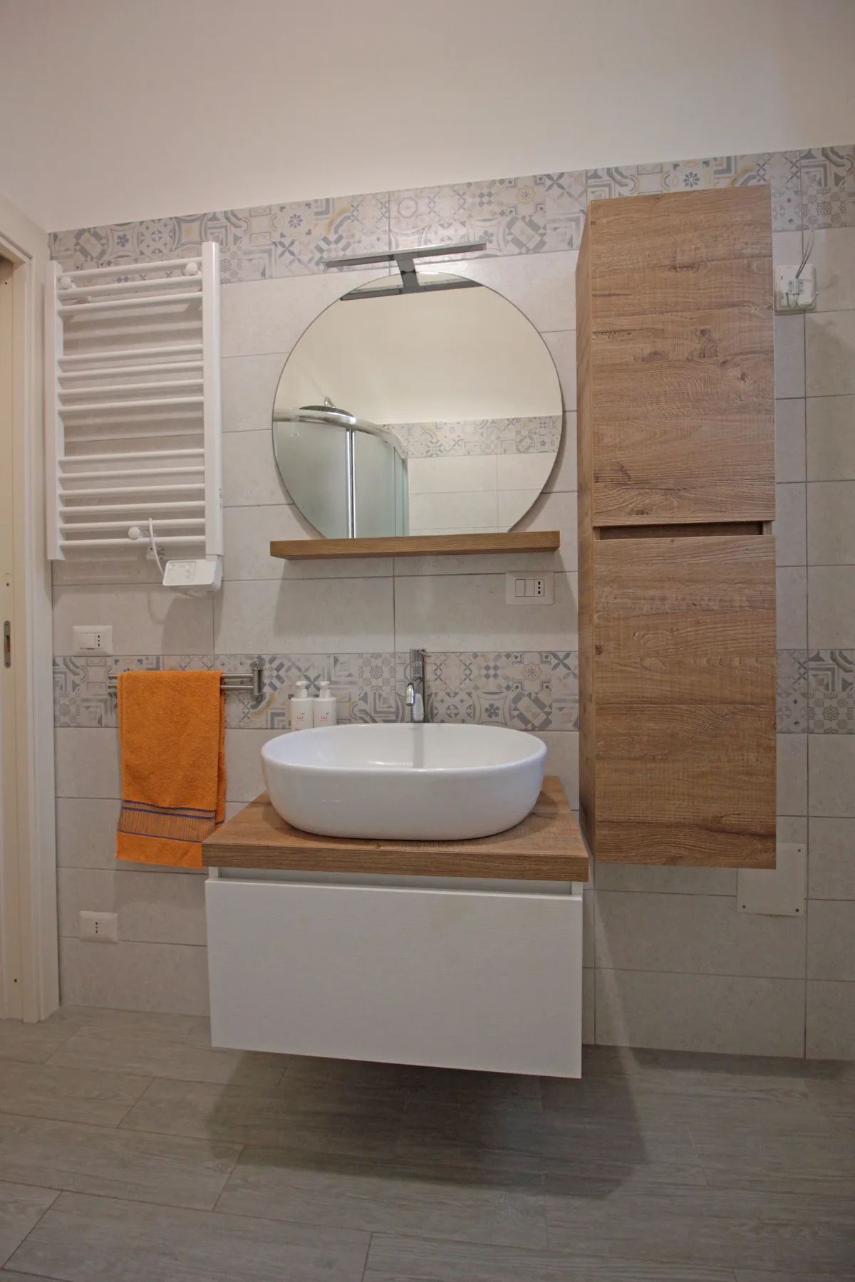 A bathroom vanity with a round mirror and wall-mounted sink.