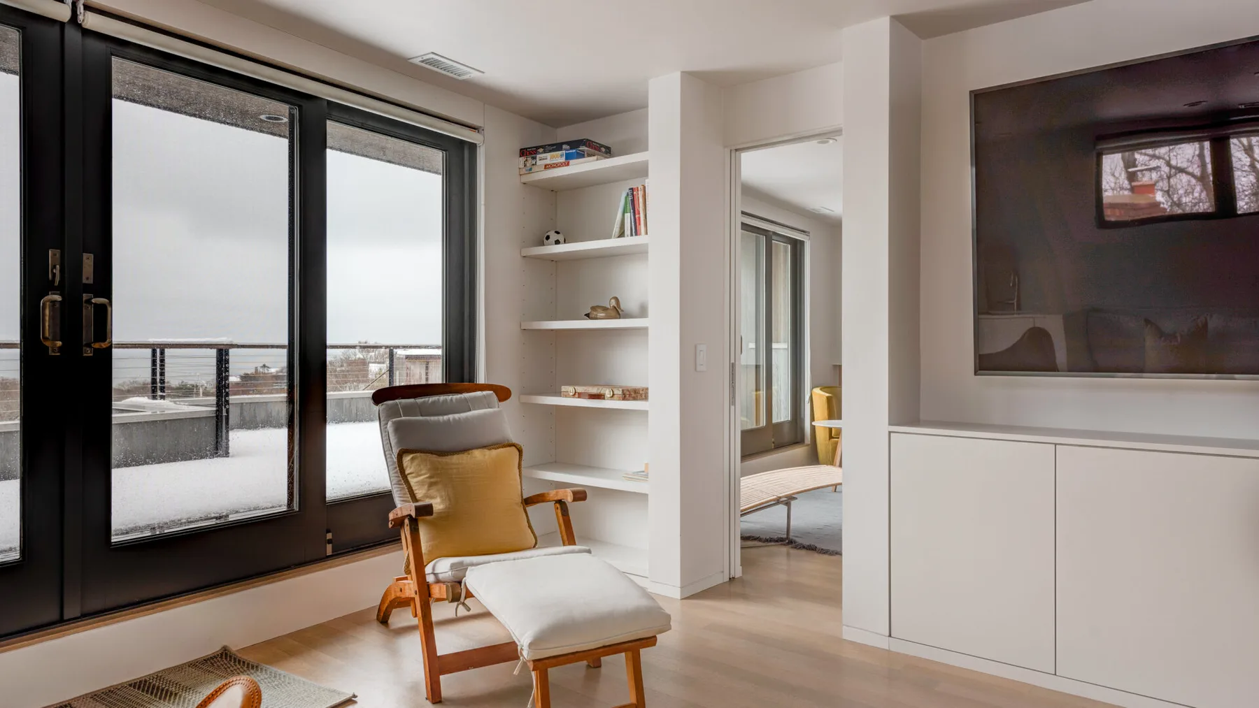 A bright living area with a lounge chair beside large glass doors and built-in shelves.