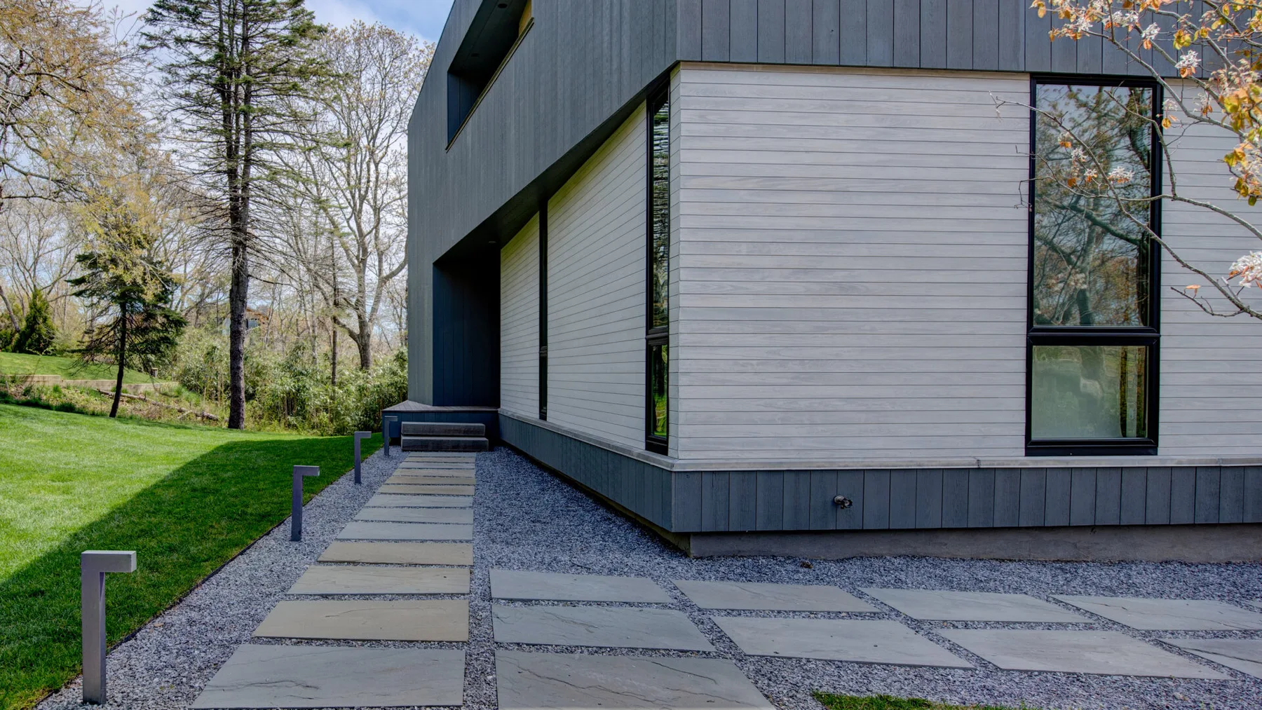 A modern house exterior borders a paved walkway and grassy yard.