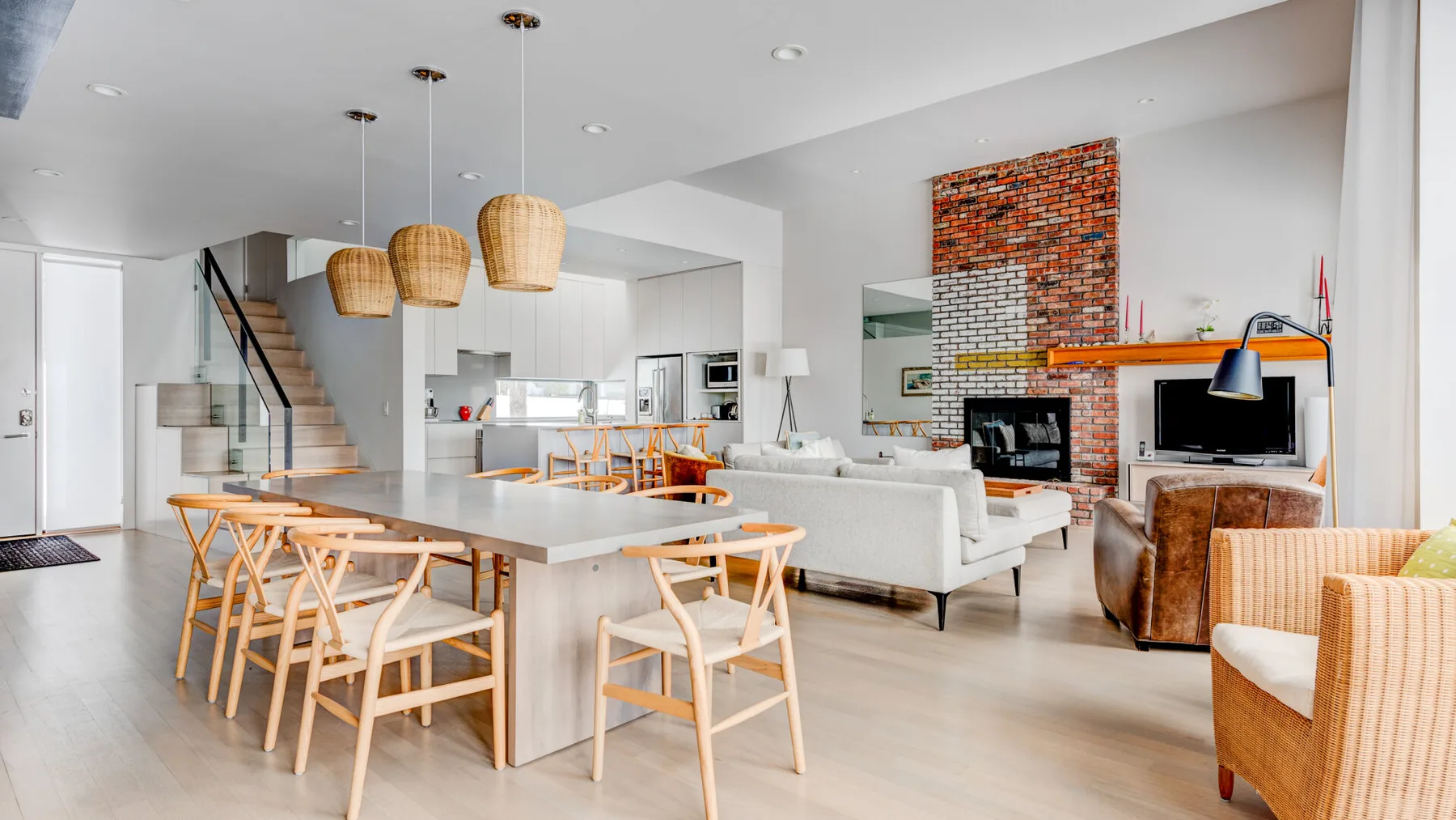 An open-plan living and dining area has a long table and seating by a brick fireplace.