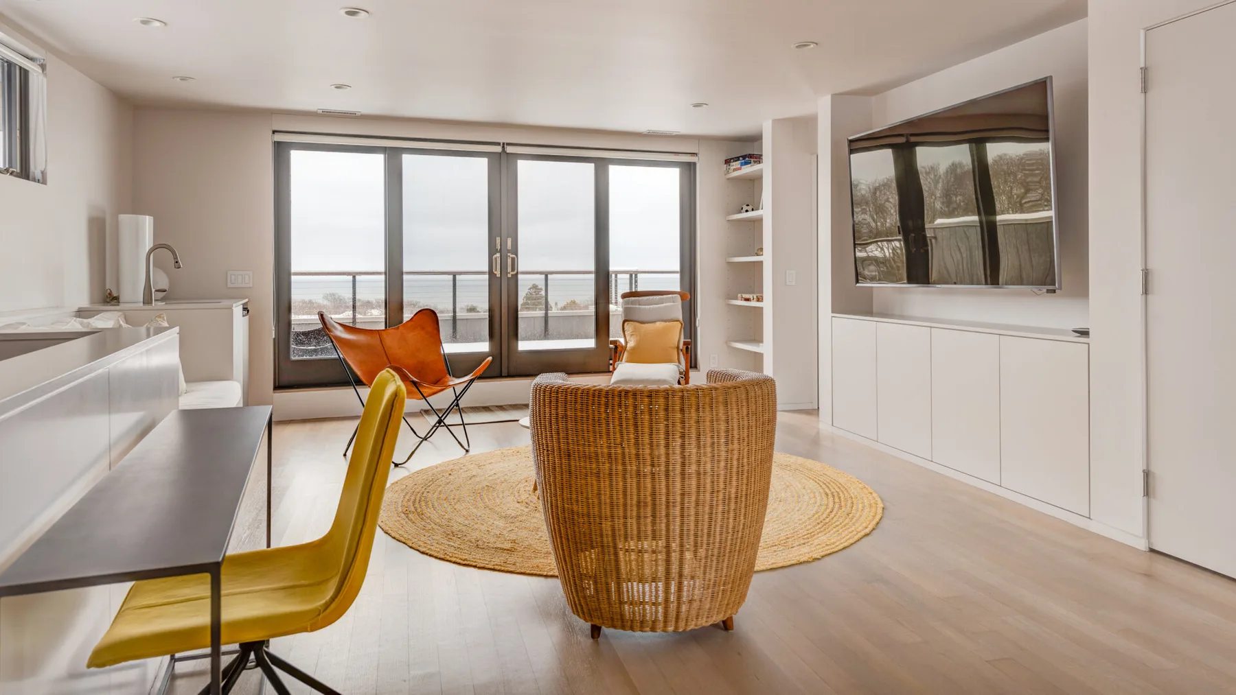 A bright living area has seating around a round rug beside large glass doors.