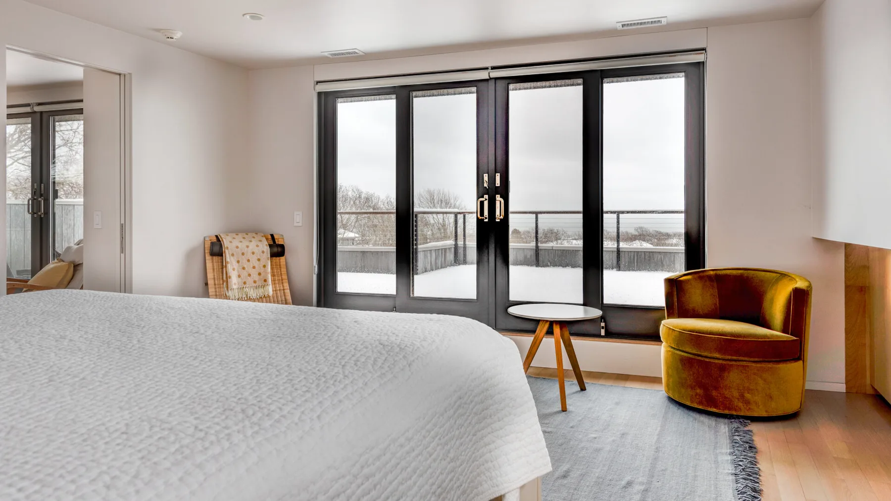 A bedroom with a bed, an armchair, and large windows overlooking a balcony.