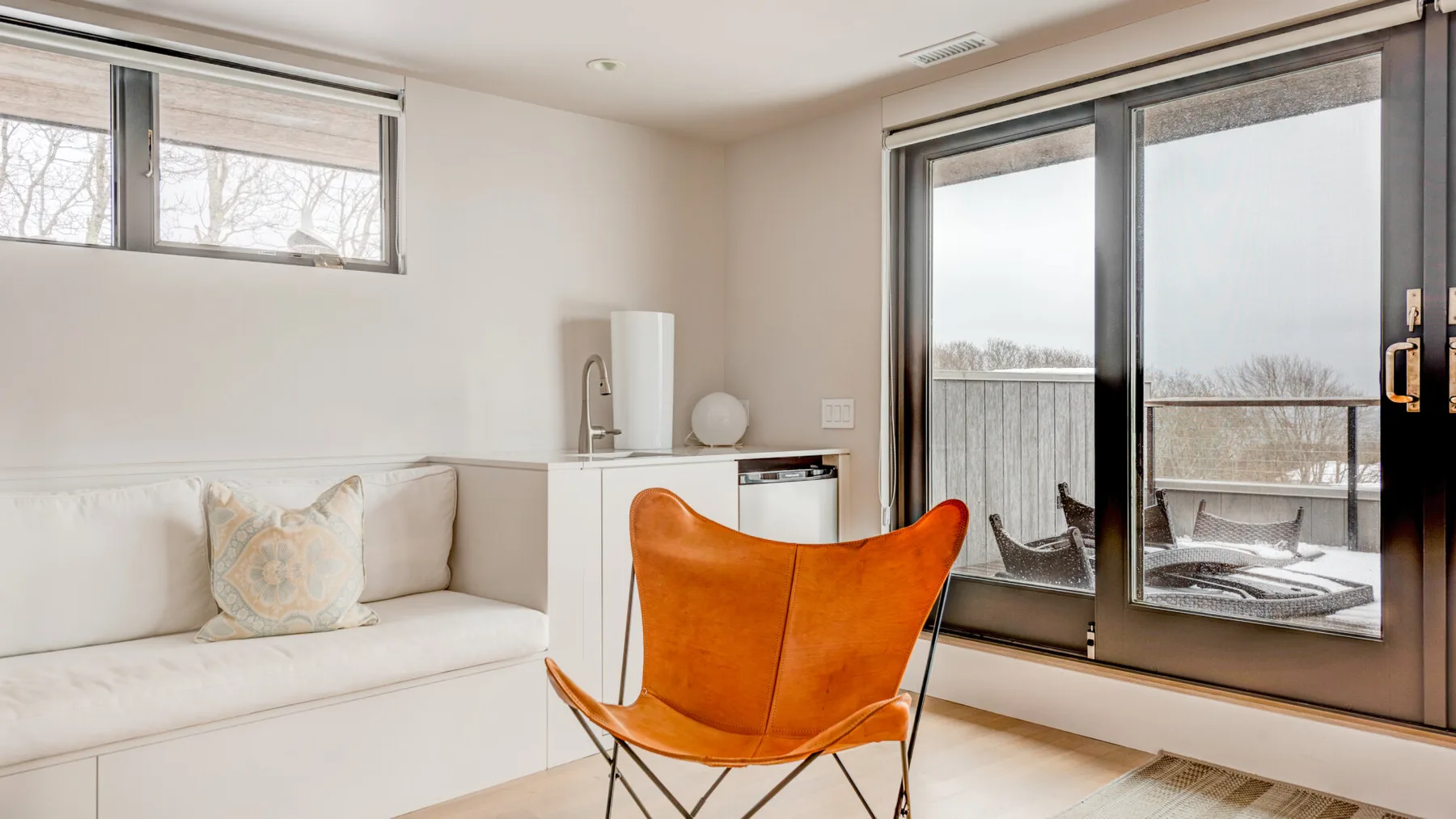 A bright sitting area with a white sofa and an orange lounge chair beside glass doors.