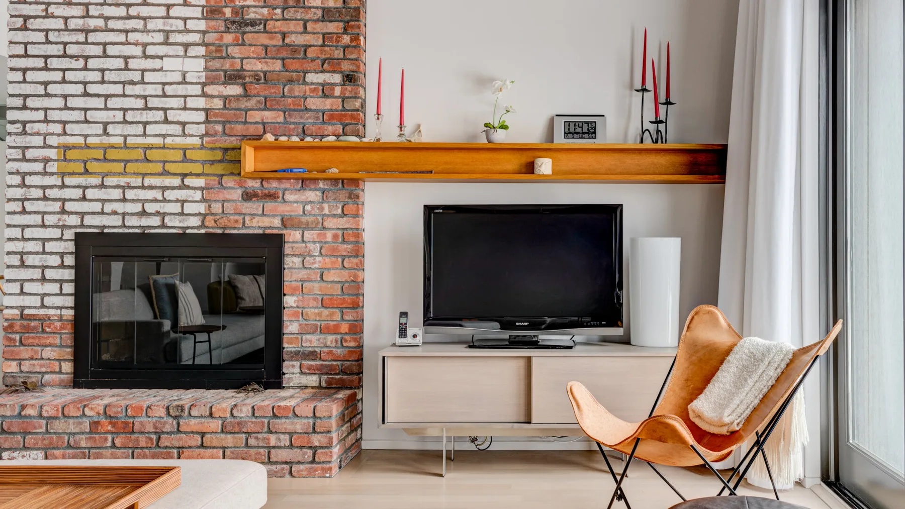 A living room with a brick fireplace, television, and seating beside a window.