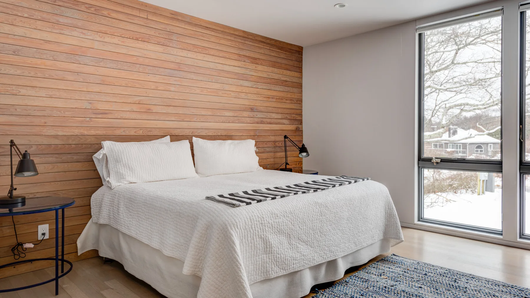 A bedroom with a bed against a horizontal wood-paneled wall and a large window.