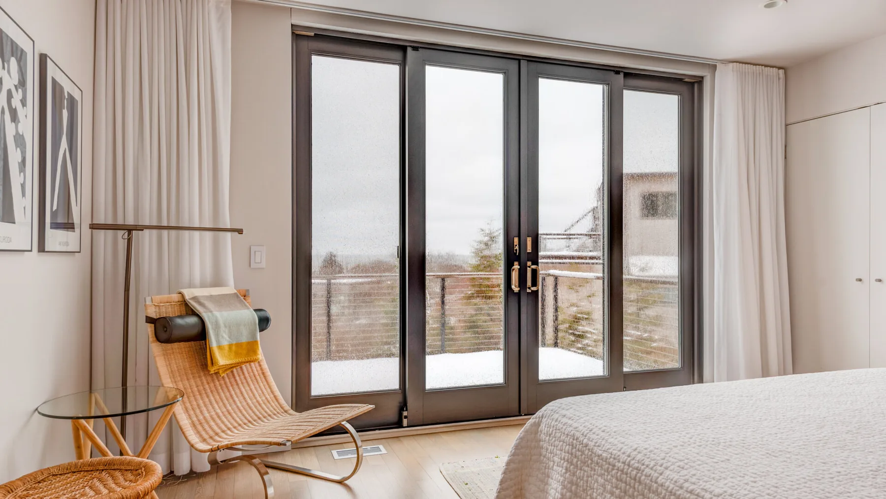 A bright bedroom with a bed beside tall glass doors and curtains.
