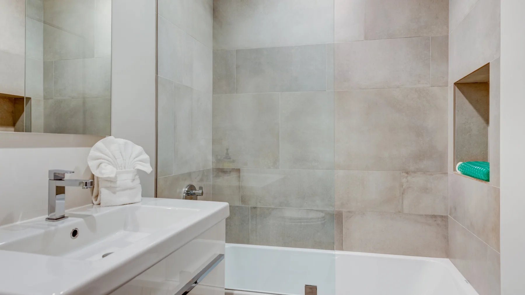 A tiled bathroom with a sink, bathtub, and folded towel.