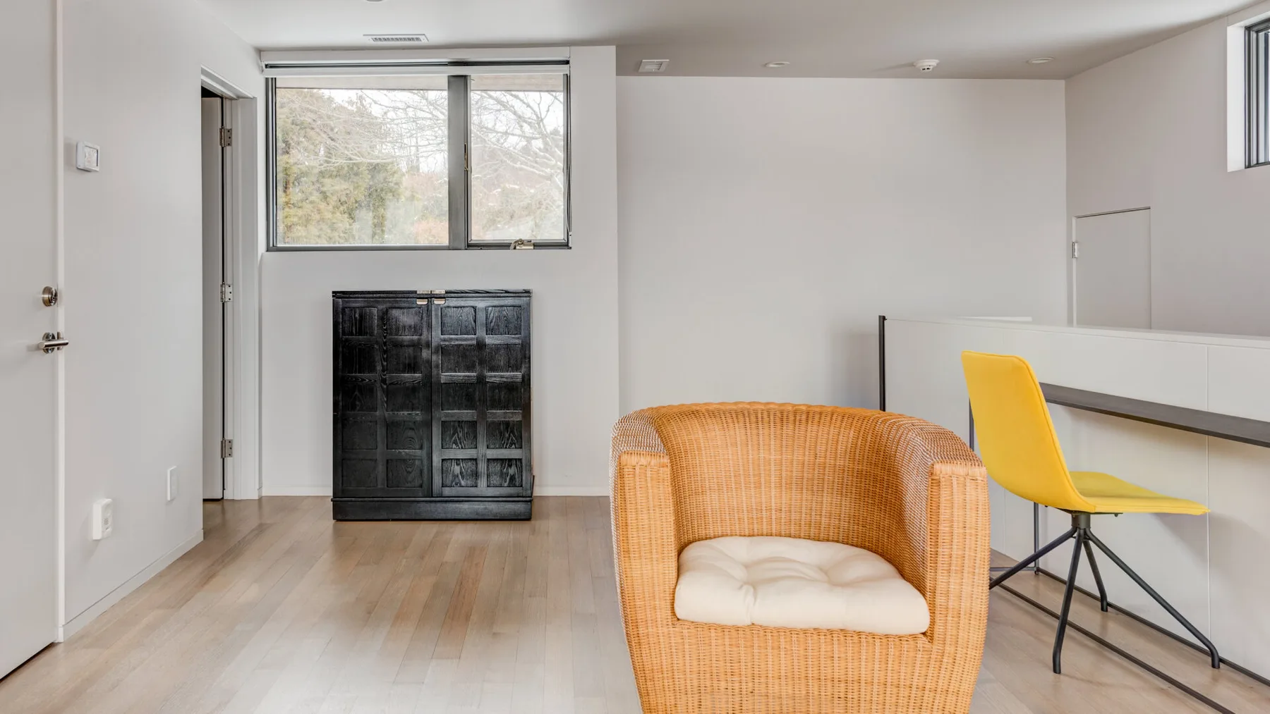 A bright room with a wicker armchair beside a counter and yellow seating.