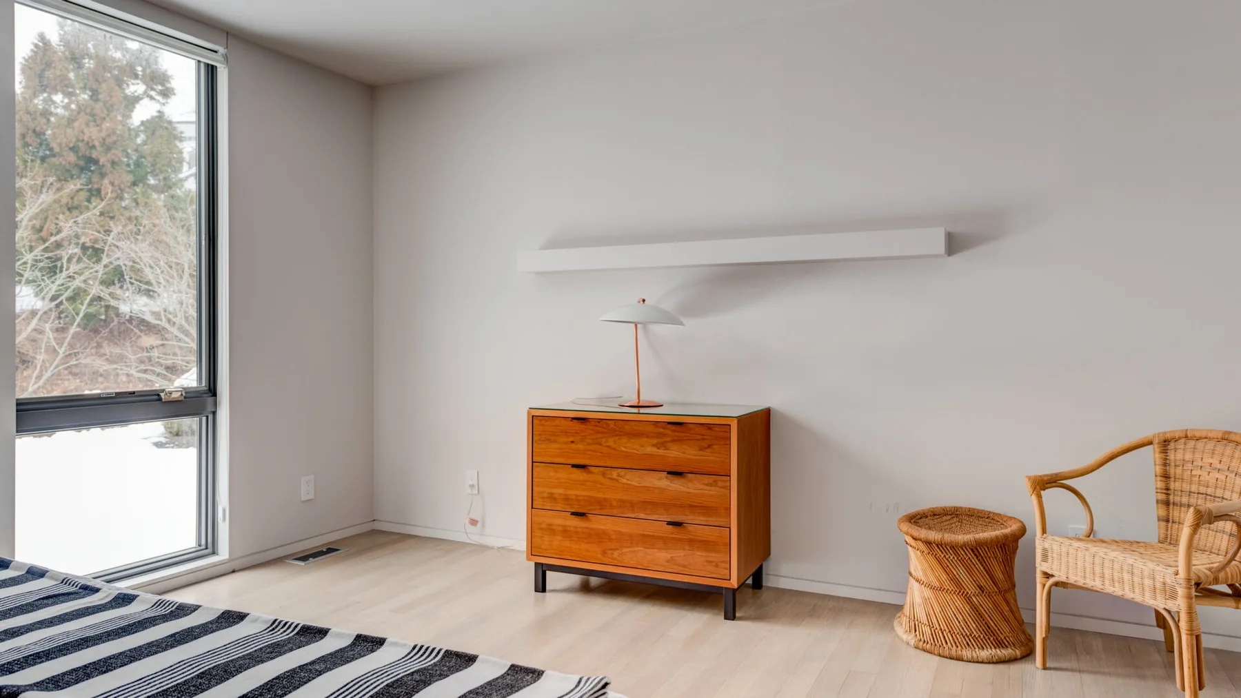 A bright bedroom with a low wooden dresser and a large window.