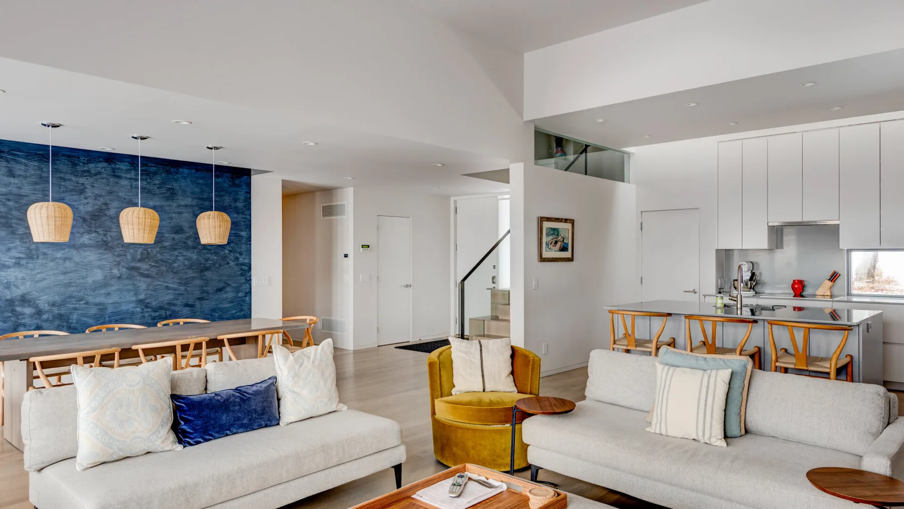 A modern living and dining area features sofas, a dining table, and a blue accent wall.