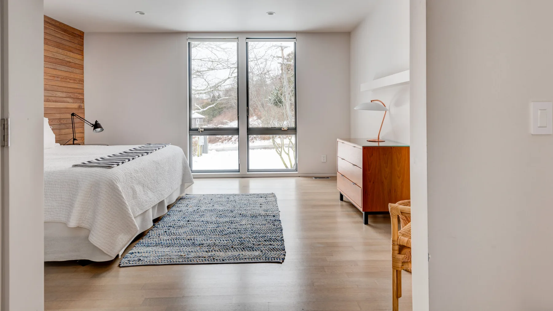 A bright bedroom with a bed, large windows, and a patterned rug.