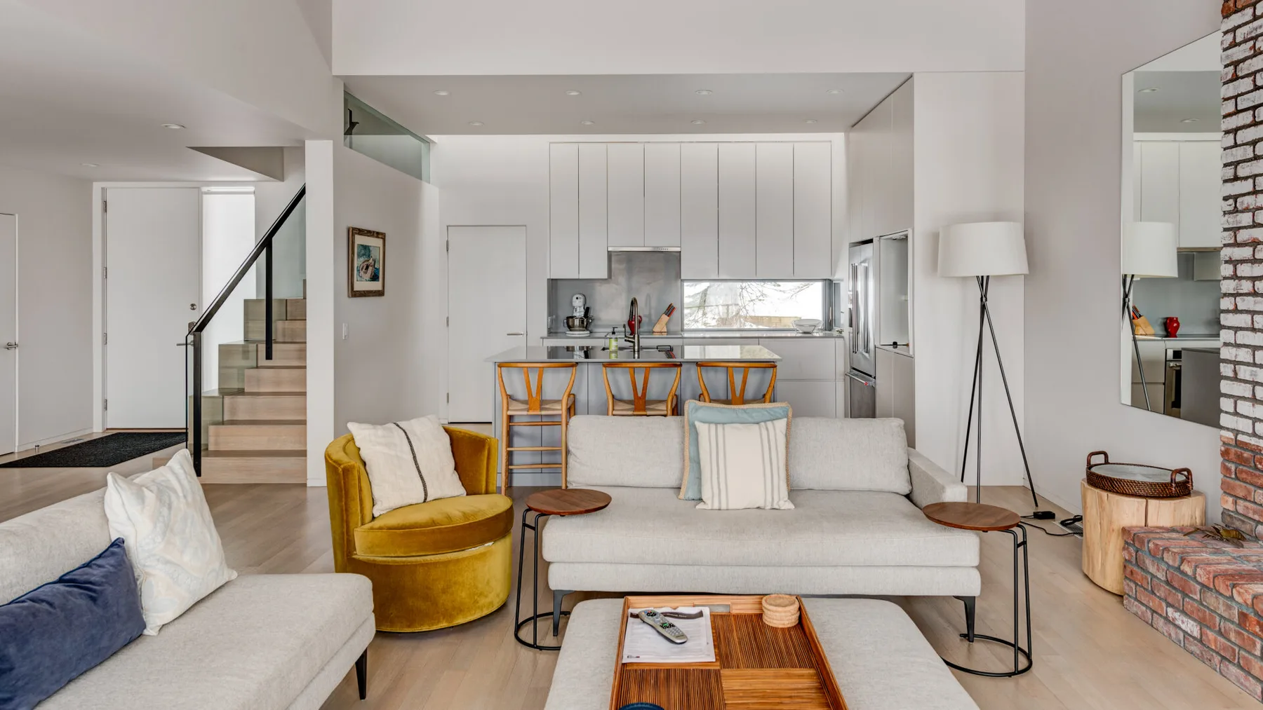 A modern living room opens onto a kitchen, with a gray sofa and yellow chair.