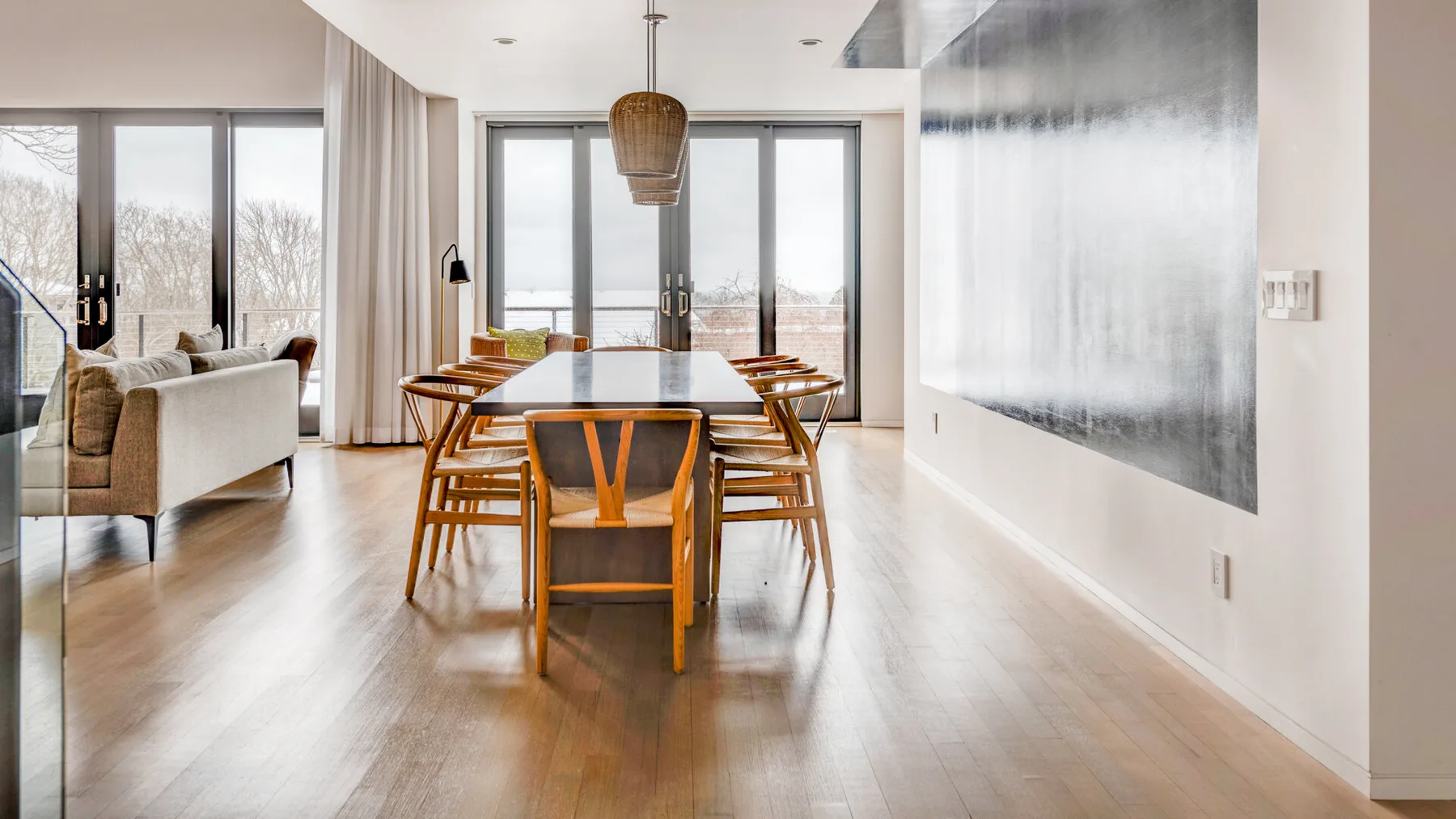 A dining area with a wooden table and chairs beside large windows.