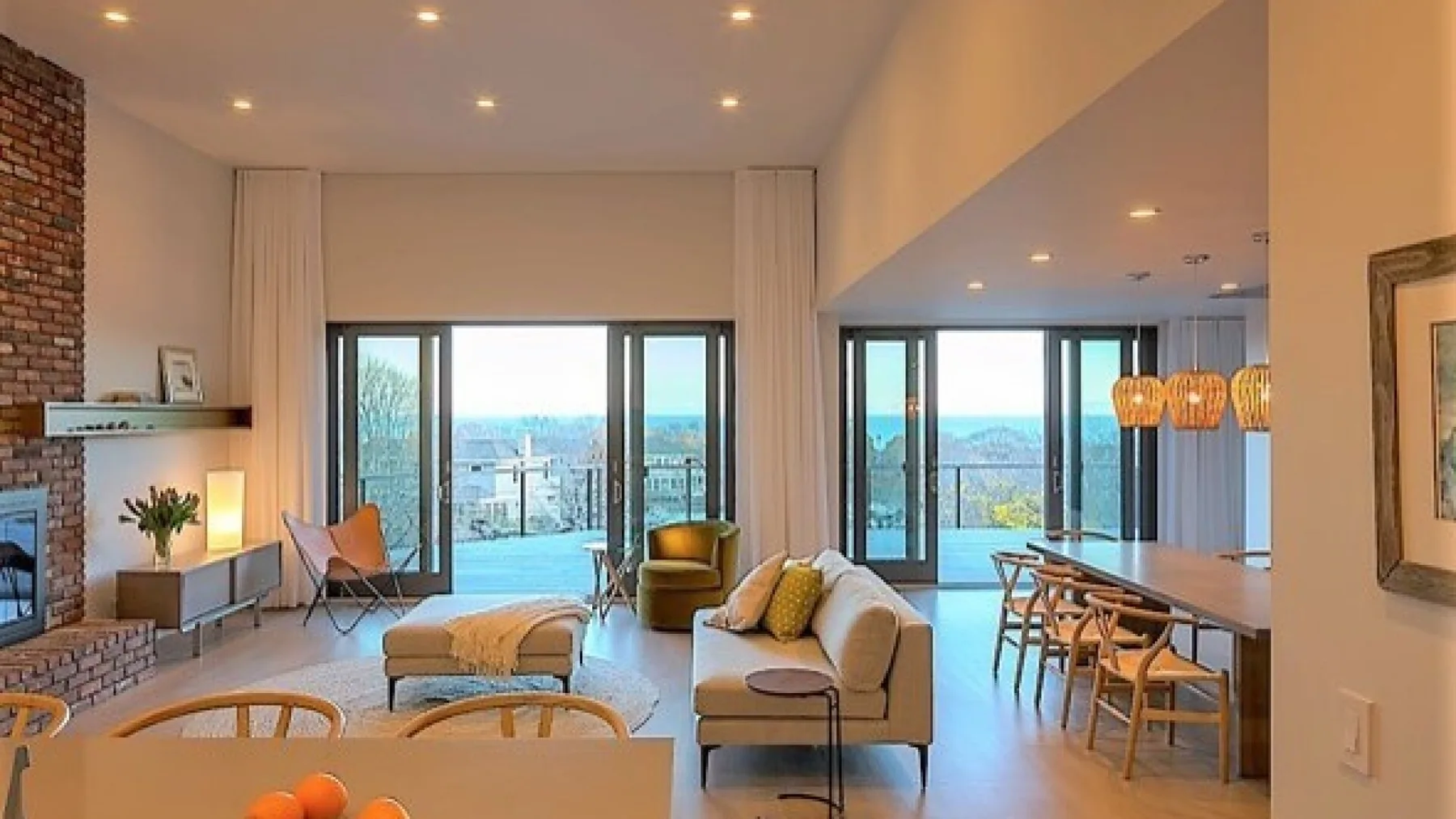 Una luminosa sala de estar de planta abierta con grandes ventanales, asientos y una mesa de comedor.