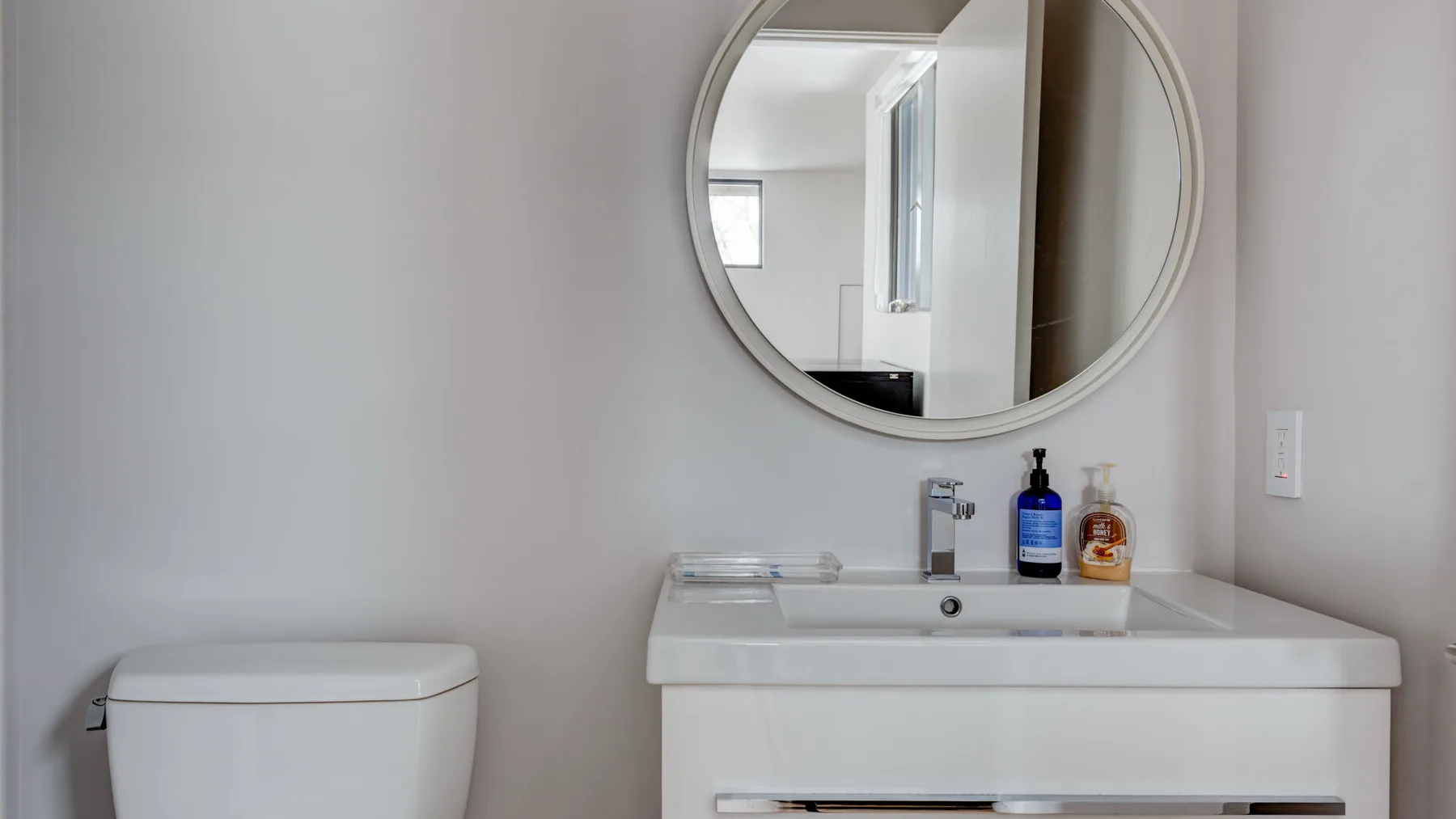 A bathroom vanity with a sink and round wall mirror.