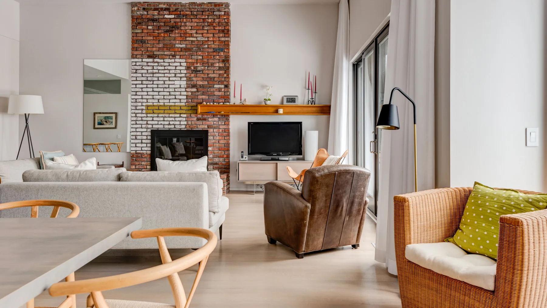 A bright living room with a brick fireplace and seating arranged around a television.