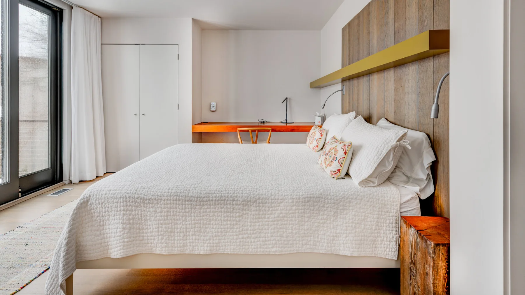 A bedroom with a large bed, a wooden accent wall, and a desk.