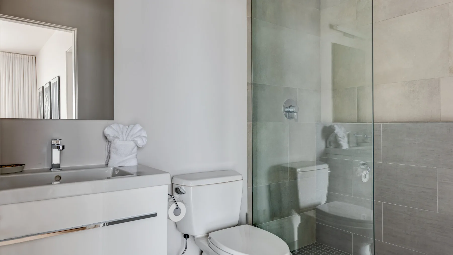 A bathroom with a sink vanity, toilet, and glass-enclosed shower.