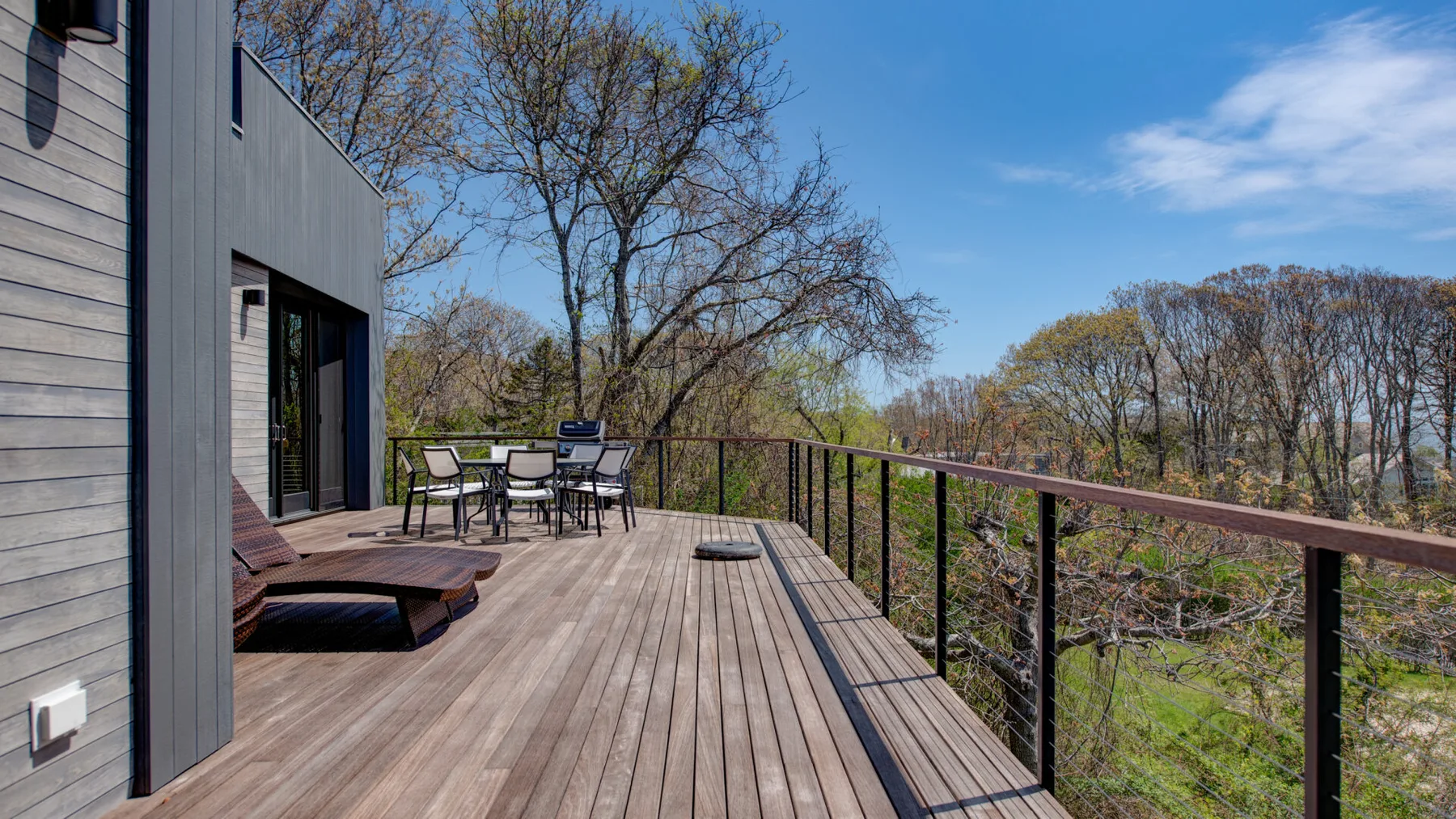 A spacious wooden deck with outdoor seating overlooks a tree-filled landscape.